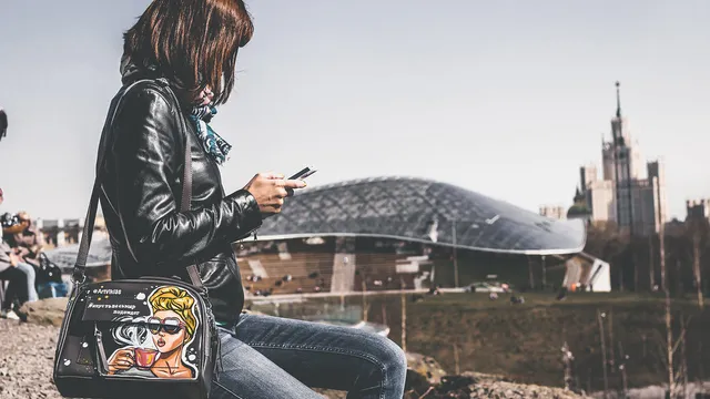 Une femme en blouson de cuir regarde son smartphone en pleine rue