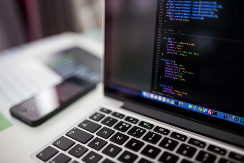 Un ordinateur portable affiche du code à côté d'un smartphone posé sur le bureau