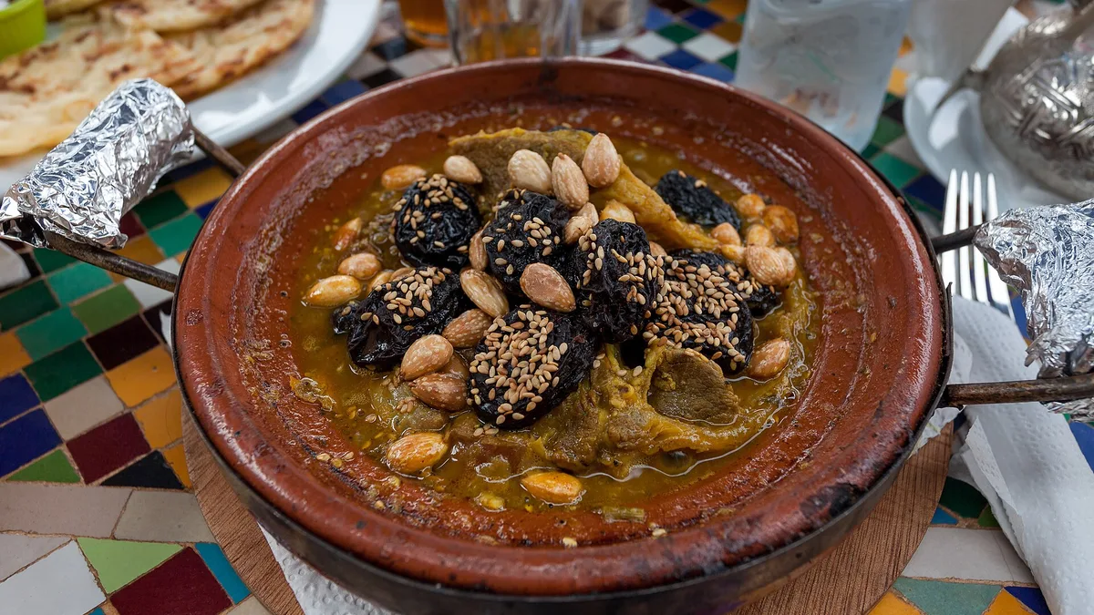 Un tajine à la viande garni de pruneaux et d'amandes, servi sur une table en zellige
