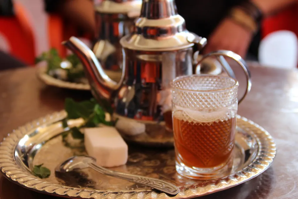 Théière marocaine en métal argenté et verre de thé à la menthe posés sur un plateau ciselé