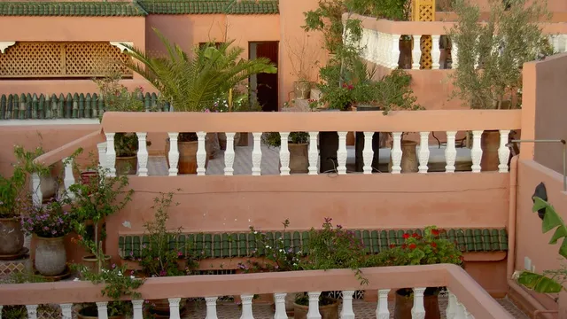 La terrasse d'un riad avec balustrades blanches, murs roses et plantes vertes