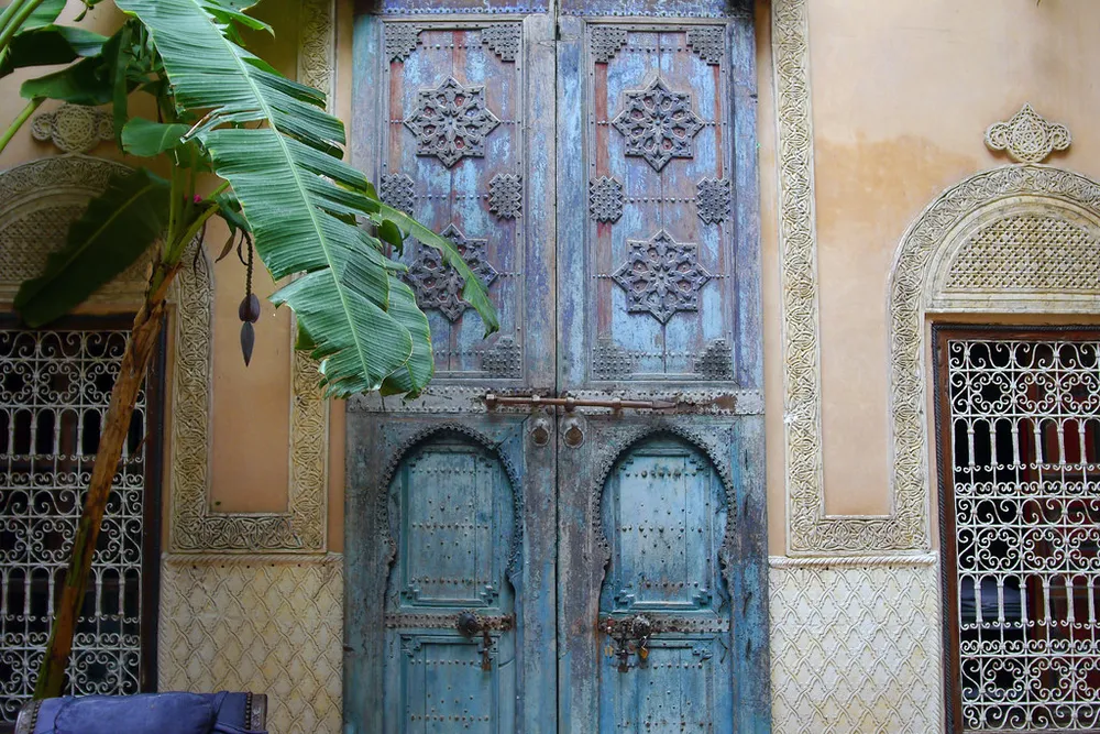 Des portes en bois bleu sculpté dans le patio d'un riad à Marrakech